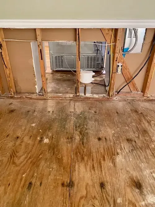 Opened wall framing above a plywood subfloor marked by water damage