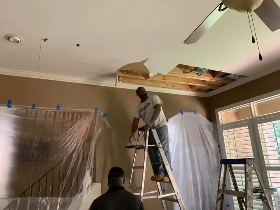 Workers open a damaged ceiling above a protected room after a leak