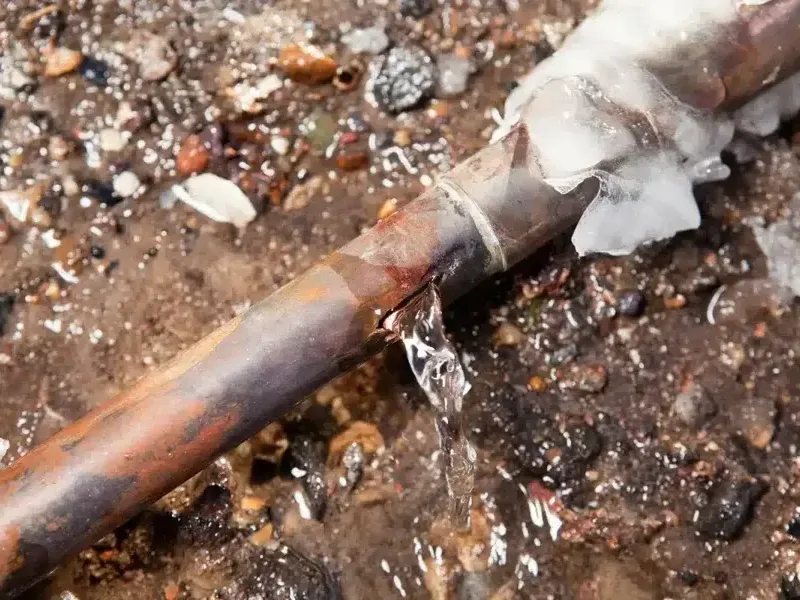Ice surrounds a split copper pipe beside water spraying from the opening