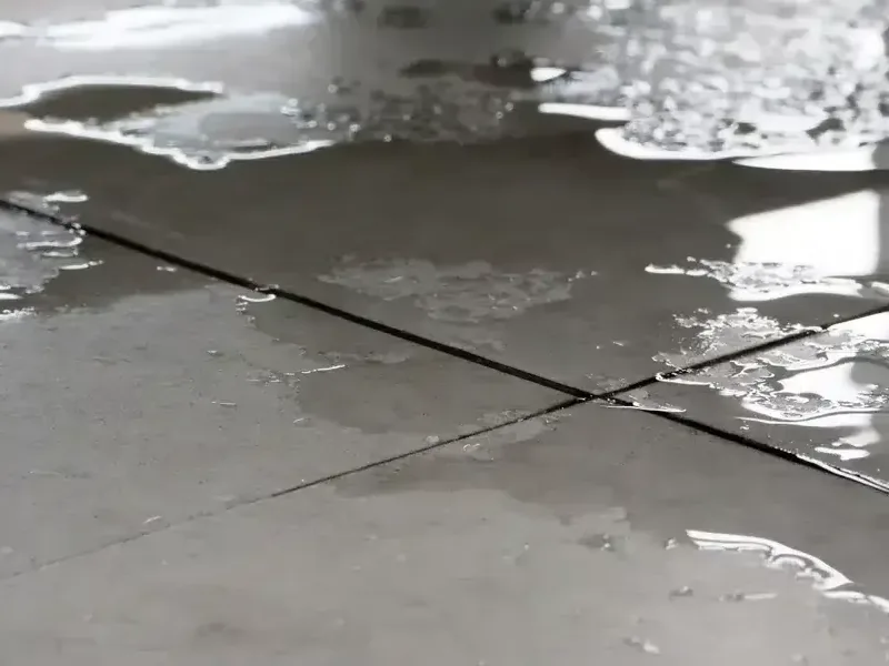 Water pools across square floor tiles and collects along the grout joints