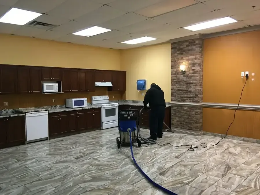 A technician extracts water from a hard floor in a shared indoor room